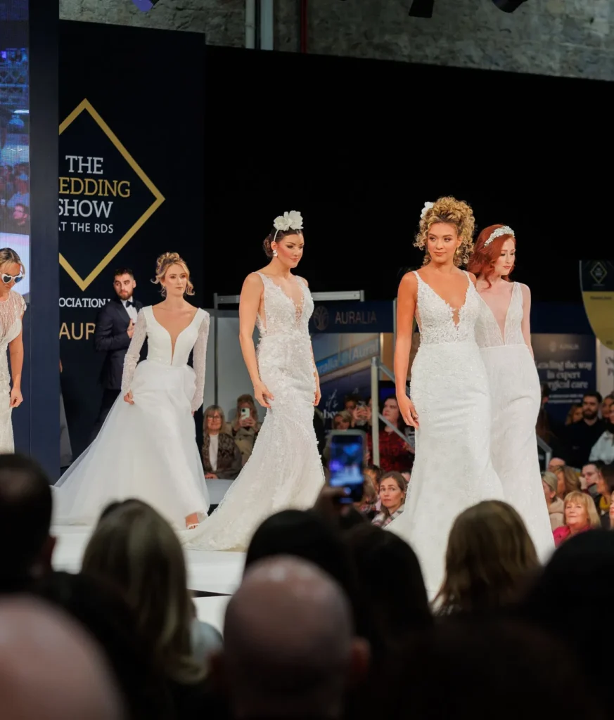 Bridal fashion show with models in elegant wedding dresses walking the runway, showcasing modern bridal designs.
