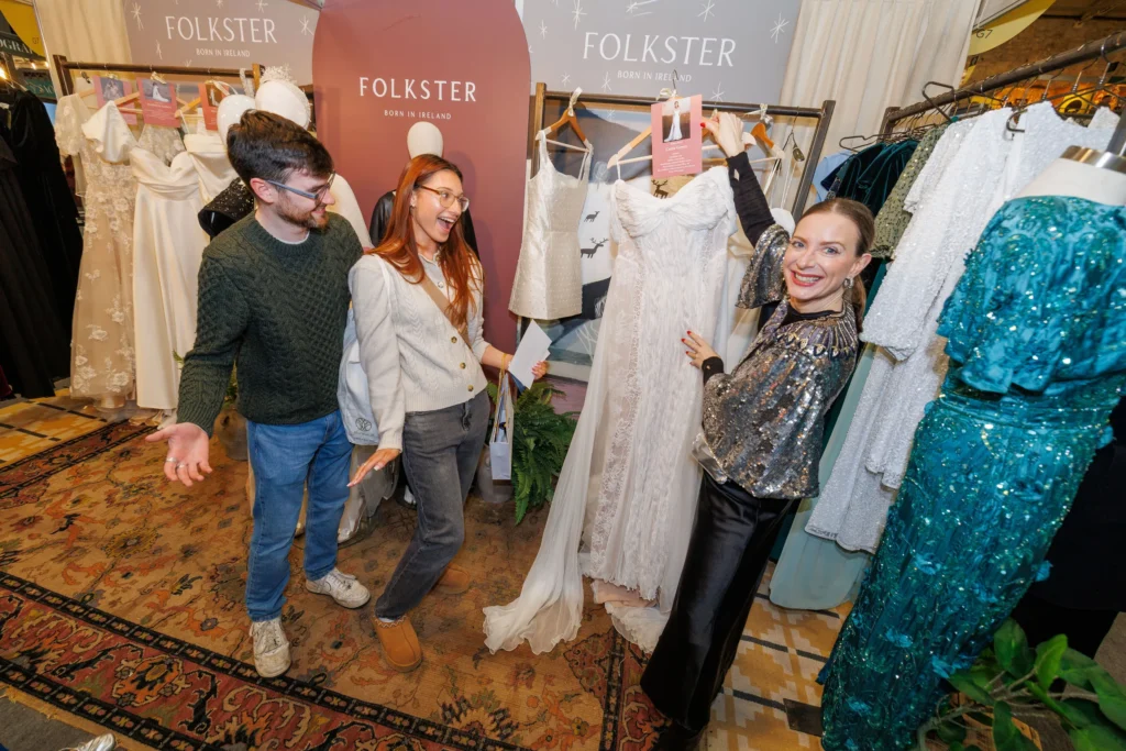 People shopping for dresses at a Folkster boutique, showcasing elegant white gowns and excited customers.